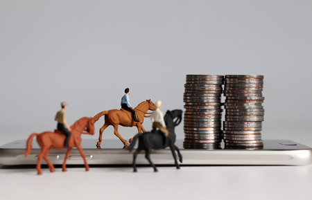 Miniature man riding a horse. Smartphone and coin stacks.の写真素材