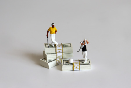 Miniature people playing golf with wad of $ 100 bills.の写真素材