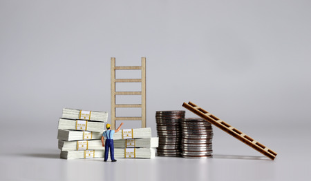 Pile of bills and coins. Miniature people and wooden ladders.の写真素材