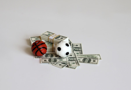 A miniature soccer ball and a basketball ball with bills.の写真素材