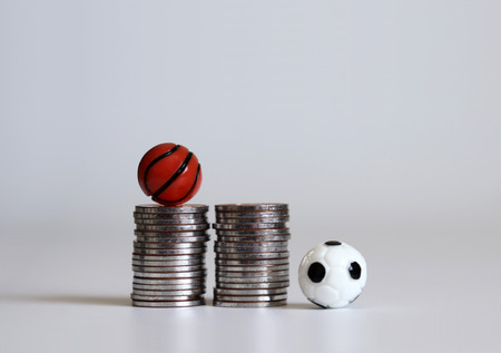 A miniature soccer ball and a basketball ball with pile of coins.