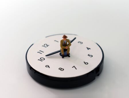 The concept of time management. A miniature man sitting on a clock needle.