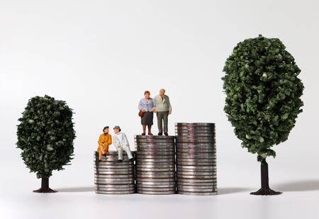 Old age miniature people on a pile of coins between miniature trees.