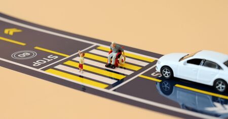 A miniature child with a hand raised and a miniature man in a wheelchair crossing a crosswalk.の写真素材
