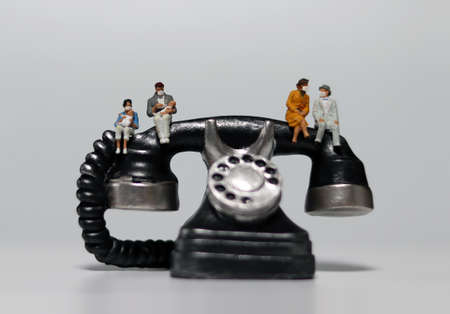 Miniature people wearing masks and sitting on miniature phones. Concepts that encourage social distance and non-face-to-face contact.の写真素材