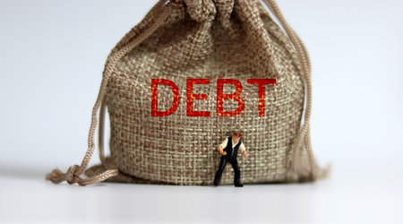 A bundle bearing the word DEBT and a miniature man standing. The concept of increasing household debt.の写真素材