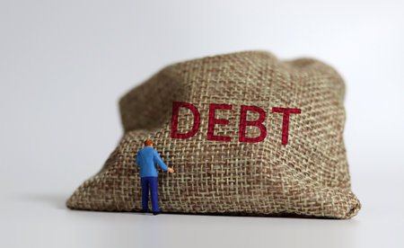 A bundle bearing the word DEBT and a miniature man standing. A warning concept about the risk of increasing debt.の写真素材