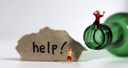 The concept of warning against the increasing risk of domestic violence. Miniature child with a paper written'help' and a miniature woman sitting on a bottle.の写真素材