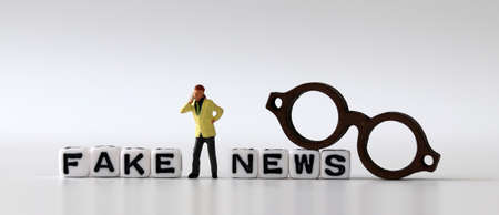 White dice and'FAKE NEWS' with News, solution and business concepts on white background. White cube, miniature glasses and miniature people.の写真素材