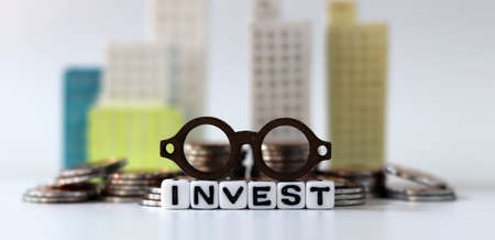 A miniature eyeglasses on White cube bearing the word 'INVEST' with a bundle. The concept of real estate investment.の写真素材