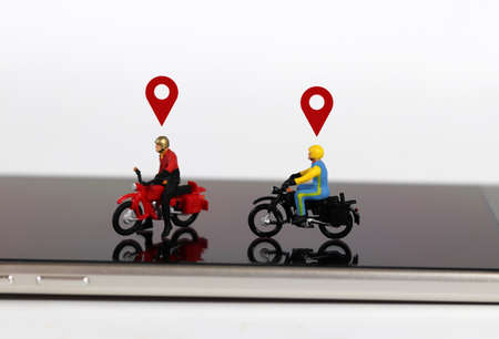 Smartphones and miniature people. Two miniature motorcycle riders with two red location mark on the...