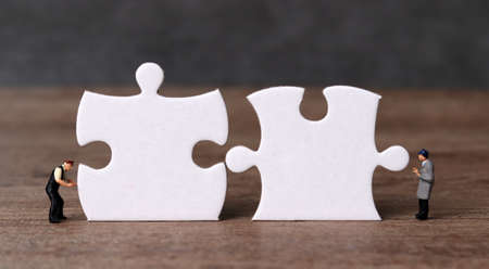 White puzzle pieces and miniature people with business concept. Miniature people working on two pieces of the puzzle.の写真素材