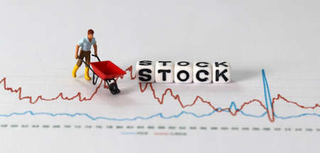 Business concept with graphs and miniature people. White cube with 'STOCK' text.
