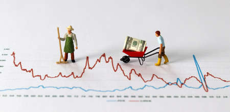 Business concept with graphs and miniature people. A miniature man carrying dollars in the cart on a...