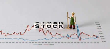 Business concept with graphs and miniature people. White cube with 'STOCK' text.