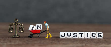 A miniature man who takes out "IN" from "INJUSTICE" and moves it to a cart. The concept of the importance of justice.の写真素材