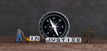 A miniature man who takes out "IN" from "INJUSTICE" and moves it to a cart and scale.の写真素材