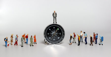 A miniature man is standing on a compass and miniature people are standing around him. Concepts related to leadership.の写真素材