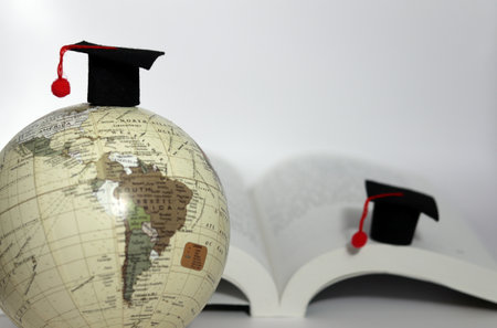 A globe with a school cap and a school cap on a book. Global education concept.