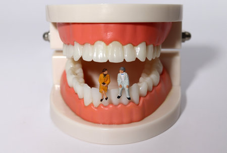 Two miniature old men sitting on a model of their teeth. The burden of dental expenses for the...