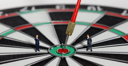 Business goals and concepts for achievement and victory. Miniature entrepreneurs agonizing over dart boards with red dart arrows hitting the center.の写真素材