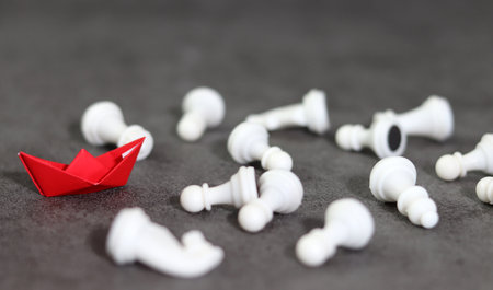 Red paper boats on the dark background and fallen white chess horses. Concept for competition and strategy.の写真素材
