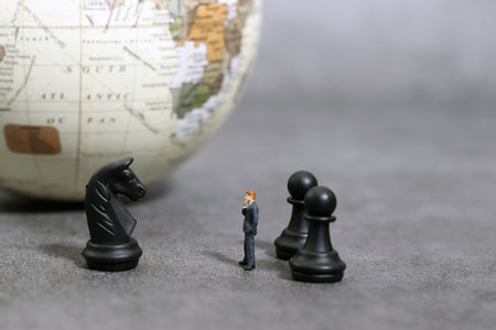 A miniature businessman facing chess horses against the backdrop of the earth. Global business concept.の写真素材