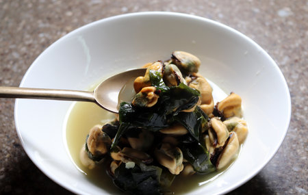 Beat the mussel soup in a white bowl with a spoon. Mussel soup boiled with Korean seaweed.