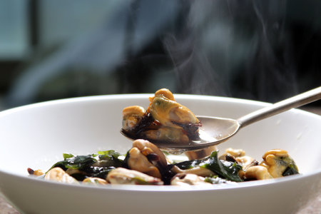 Beat the mussel soup in a white bowl with a spoon. Mussel soup boiled with Korean seaweed.の写真素材