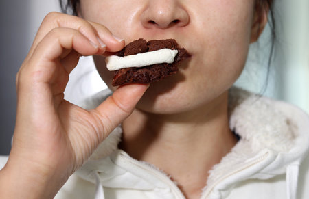 A young woman eating a chocolate cookie with marshmallows.の写真素材