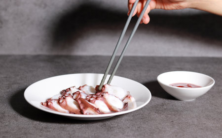 Pick up an octopus on a white plate with chopsticks. Fresh seafood dishes and red chili-pepper paste.の写真素材