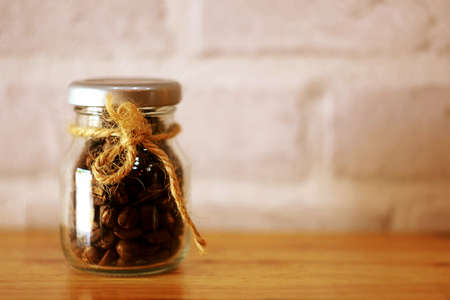 this is a dark roasted coffee beans in glass container on wooden table, brick backgroundの写真素材