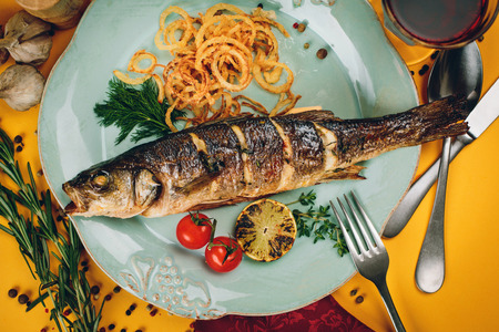 Plate of grilled fish with squid and tomatoes on a yellow background