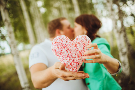 Happy and young couple in love kissing and holding a heart in a birch groveの写真素材