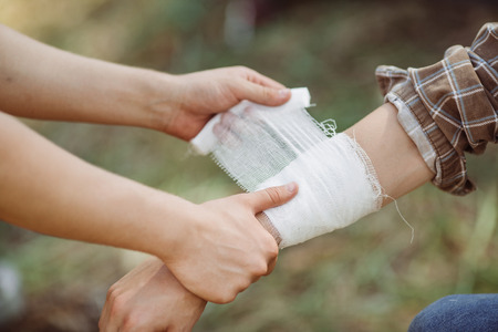 A person wrapping his friends injured arm in gauze