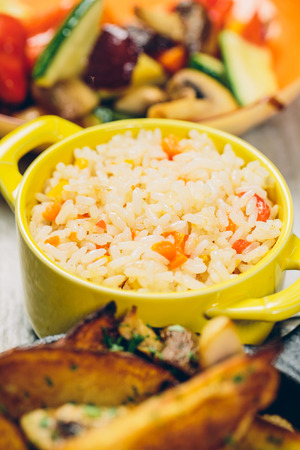 A delicious bowl of seasoned rice on a background of potatos and vegetablesの写真素材