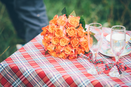 A bouquet of orange and pink flowers with two wine goblets lying on a wedding tableの写真素材