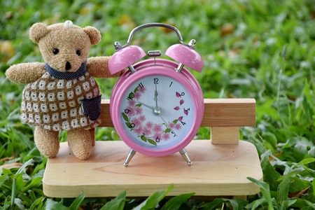 Pink alarm clock outdoors sitting in chair on the break with bear toysの写真素材
