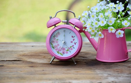 Alarm clock and white flowers in pink vase on brown wood table in morning timeの写真素材