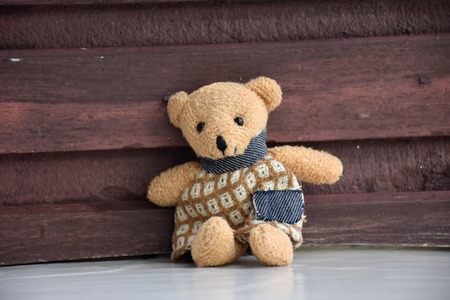 One cute toy bear sitting on the white floor and brown wood backgroundの写真素材