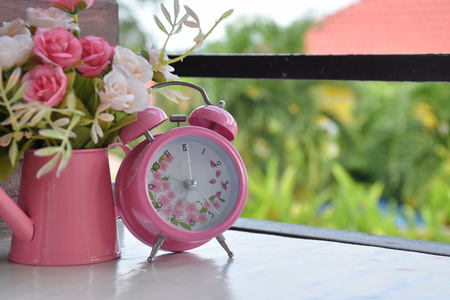 Pink Alarm clock and rose flowers in vase on white  table in morning timeの写真素材