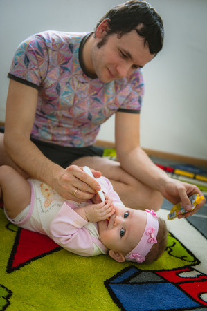 Papa feeds child with spoon. Image of young dad with cute little daughter on floor at home. Father and baby girl indoor.の写真素材