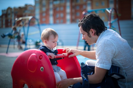 Image of cute little daughter with her young dad. Father and baby girl outdoor. Child plays on playground.の写真素材