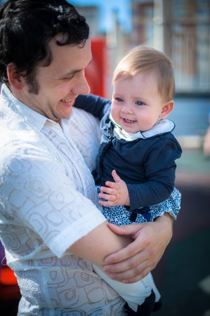 Image of cute little daughter in young dad's hands. Father and baby girl outdoor. Child plays on playground.の写真素材
