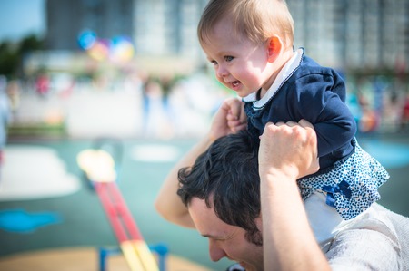 Image of cute little daughter in young dad's hands. Father and baby girl outdoor. Child plays on playground.の写真素材