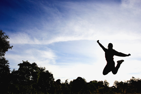 Silhouette of girl jumping in blue sky.の写真素材