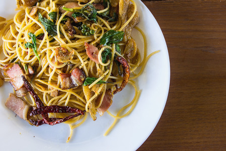 Spicy spaghetti with bacon and basil in the white dish on wooden backgroundの写真素材