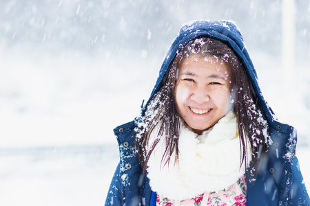 Asian woman smiling and feeling happy to travel the snow in winter in Gumma, Japan. Snow falling on her face and clothes.の写真素材