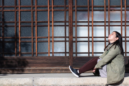 The Asian woman is sitting and resting, looking up in the sun at the Japanese-style house in the morning.の写真素材