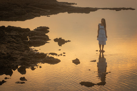 Asian woman standing in the sea at sunrise. Process in retro and vintage style and add noise grain for looking old film.の写真素材
